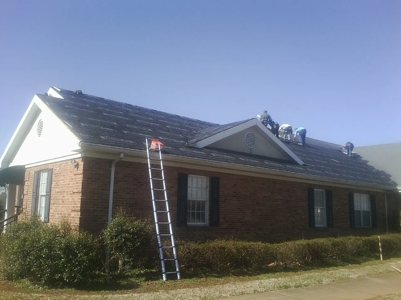 Crew tearing shingles off a brick ranch roof with a ladder set — Metal Roof Repair work by our crew in Trumbauersville