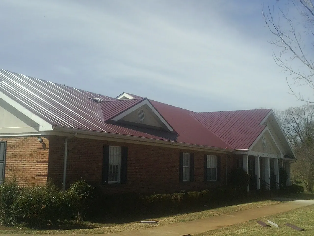 Red metal roof with gabled entries on a long brick building, from a Hail Damage Roof Repair job in Trumbauersville