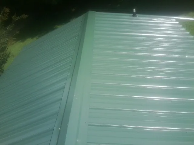 New green metal panels meeting at the ridge of a roof — Flat Roof Repair work by our crew in Trumbauersville