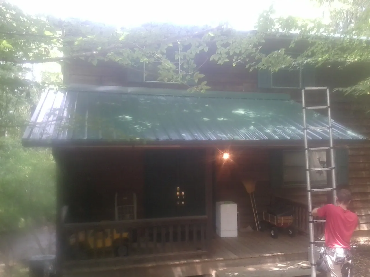 Worker on a ladder at the green porch roof of a wooded cabin in Trumbauersville