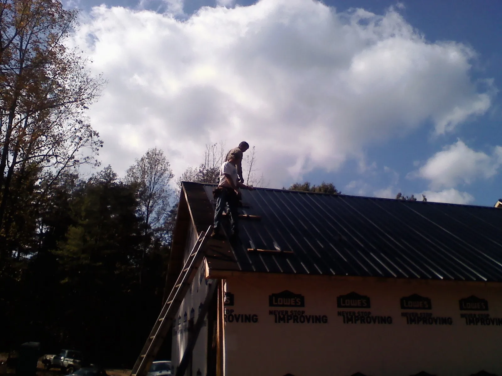 Roofer fastening dark metal panels high against a cloudy sky, from a Roof Inspection job in Trumbauersville