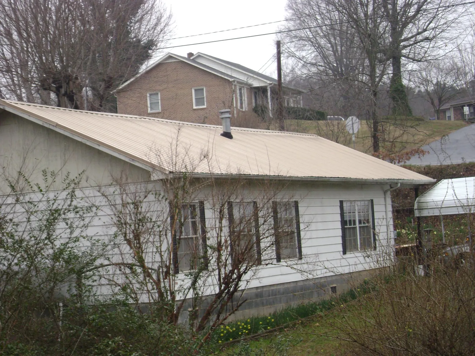 Tan metal roof on a white sided house set into a hillside — Commercial Roofing by Roofing Brothers in Trumbauersville